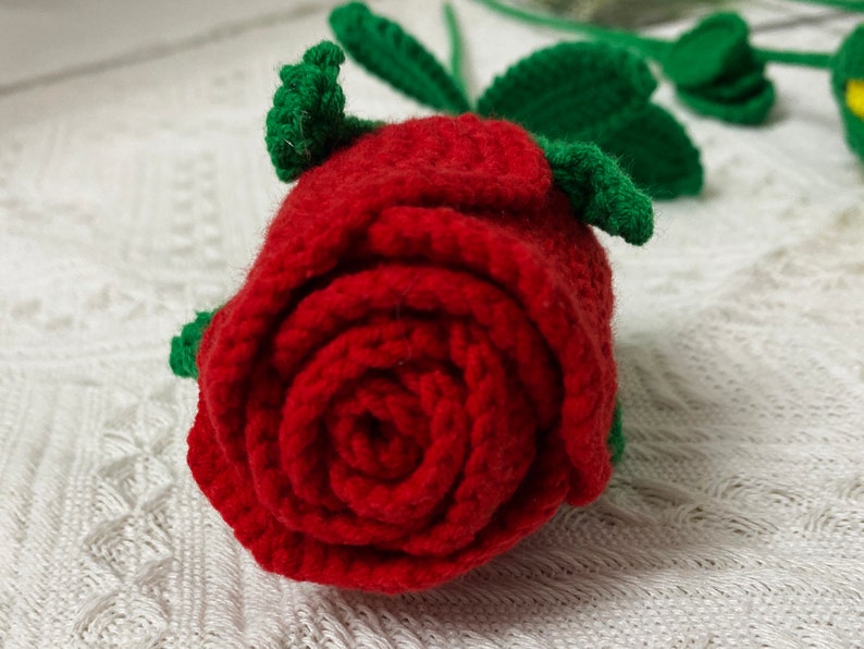 May include: A red crocheted rose with green crocheted leaves. The rose is made of yarn and is a handmade craft.