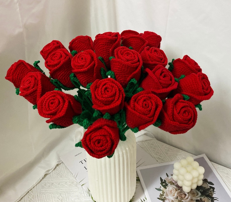May include: A bouquet of crocheted red roses with green stems and leaves. The roses are arranged in a vase.