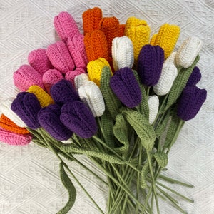 May include: A bouquet of crocheted tulips in various colors, including purple, pink, white, orange, and yellow. The tulips have green stems and leaves.