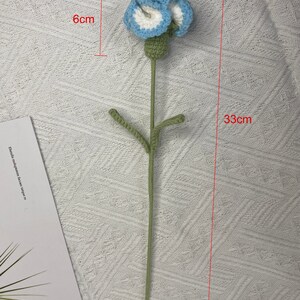 May include: A crocheted flower with blue and white petals and green leaves on a green stem. The flower is 6 inches wide and the stem is 33 inches long.