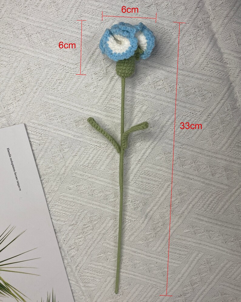 May include: A crocheted flower with blue and white petals and green leaves on a green stem. The flower is 6 inches wide and the stem is 33 inches long.