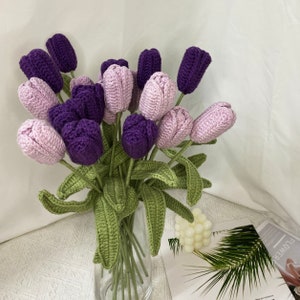 May include: A bouquet of crocheted purple and light pink tulips with green leaves in a clear glass vase.