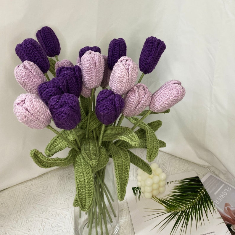 May include: A bouquet of crocheted purple and light pink tulips with green leaves in a clear glass vase.