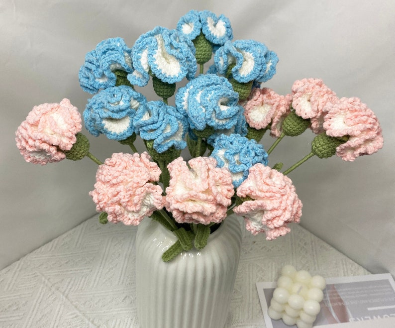 May include: A bouquet of crocheted carnations in a white vase. The carnations are pink and blue.