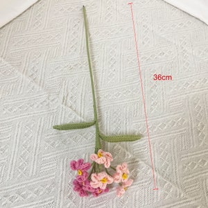 May include: A handmade crochet flower stem, approximately 14 inches long, featuring pink and light pink flowers with yellow centers. The stem and leaves are green. The flower is a decorative item.