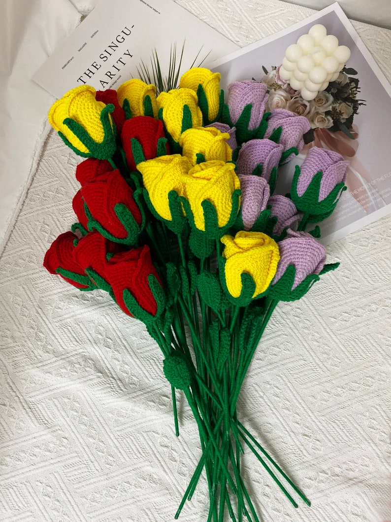 May include: A bouquet of crocheted roses in red, yellow, and purple. The roses are arranged in a fan shape and have green stems.