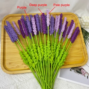 May include: A bunch of crocheted lavender flowers in shades of purple, deep purple, and pale purple. The flowers are arranged in a bouquet and have green stems.