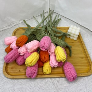 May include: A bouquet of crocheted tulips in pink, yellow, and orange. The tulips are arranged on a wooden tray.