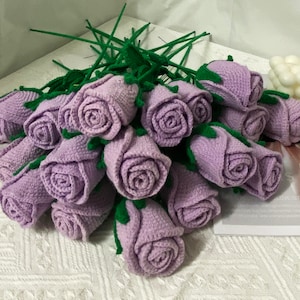 May include: A bouquet of crocheted lavender roses with green stems. The roses are arranged in a circular pattern and are tied together with a green ribbon.