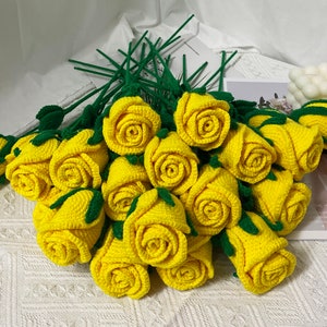 May include: A bouquet of crocheted yellow roses with green leaves and stems. The roses are arranged in a circular shape, with the stems extending outwards.