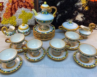 May include: A vintage Italian ceramic tea set with a teapot, creamer, sugar bowl, and six cups and saucers. The set features a floral pattern with green leaves, yellow flowers, and blue accents.