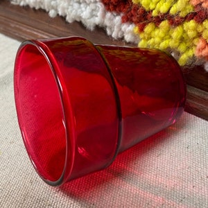 May include: A bright red glass planter, cylindrical in shape. It features a thick rim and a subtly textured interior. The glass is a deep, rich red, suitable for small plants or succulents. The planter is approximately 10 cm in diameter.
