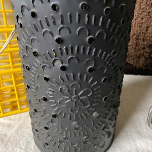 Puede incluir: Linterna de vela de metal negro con un dise&ntilde;o recortado de c&iacute;rculos, arcos y una flor. La linterna tiene un acabado desgastado.
