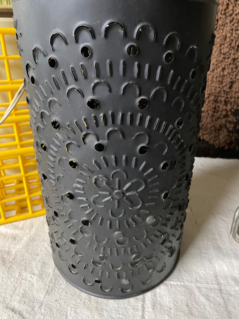 Puede incluir: Linterna de vela de metal negro con un dise&ntilde;o recortado de c&iacute;rculos, arcos y una flor. La linterna tiene un acabado desgastado.