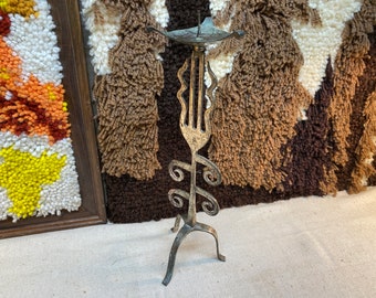 May include: A silver metal candle holder with a unique, abstract design. The holder has a tall, slender base with a decorative top that resembles a flame. The holder is made of metal and has a rustic, antique look.