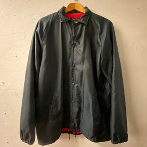 May include: A black satin baseball jacket with a red lining and a snap closure. The jacket has a classic design with a button-up front and two pockets.