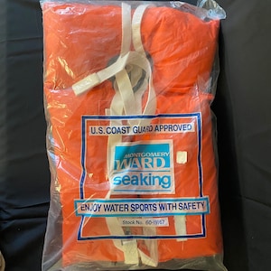 May include: Orange life jacket in a plastic bag with white straps and the text "U.S. Coast Guard Approved", "Montgomery Ward seaking", and "Enjoy Water Sports With Safety". The bag also has the text "Stock No. 60-19167".