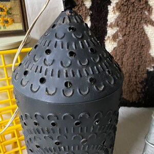 Puede incluir: Linterna de vela de metal negro con un dise&ntilde;o decorativo de corte. La linterna tiene una parte superior redonda y un lazo para colgar.