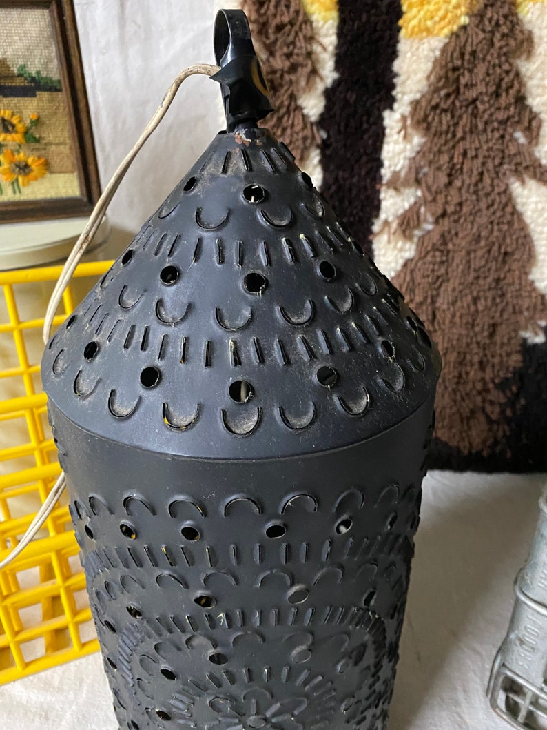 Puede incluir: Linterna de vela de metal negro con un dise&ntilde;o decorativo de corte. La linterna tiene una parte superior redonda y un lazo para colgar.