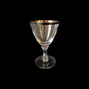 May include: A clear glass stemmed drinking glass with a gold rim. The glass has a wide bowl and a thin stem.