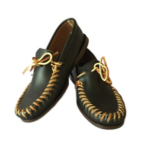 May include: A pair of black leather moccasins with tan leather laces. The moccasins have a decorative stitch pattern around the edges.