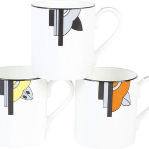 May include: Three white ceramic mugs stacked, each with a black rim and handle. The mugs feature a geometric design in grey, black, yellow, and orange. The design is on the front of each mug.