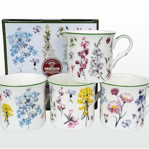 May include: Set of four white ceramic mugs with floral designs. Each mug features a different floral pattern with green, blue, pink, and yellow flowers. The mugs have a green rim and a green handle.