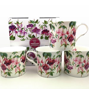 May include: Five white ceramic mugs with a fuchsia flower design in pink and purple, with green leaves. The mugs are displayed with a matching box, also decorated with the floral pattern. The mugs are suitable for tea or coffee.