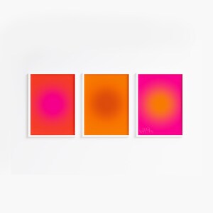 May include: Three framed abstract art prints with a gradient color scheme. The left print is red and pink, the middle print is orange, and the right print is pink and orange.
