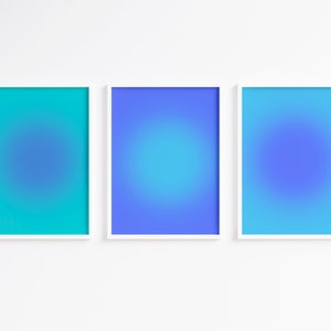 May include: Three framed art prints with a gradient design in shades of blue and teal. Each print features a central, circular blur effect within a white frame. The artwork is displayed against a white wall.