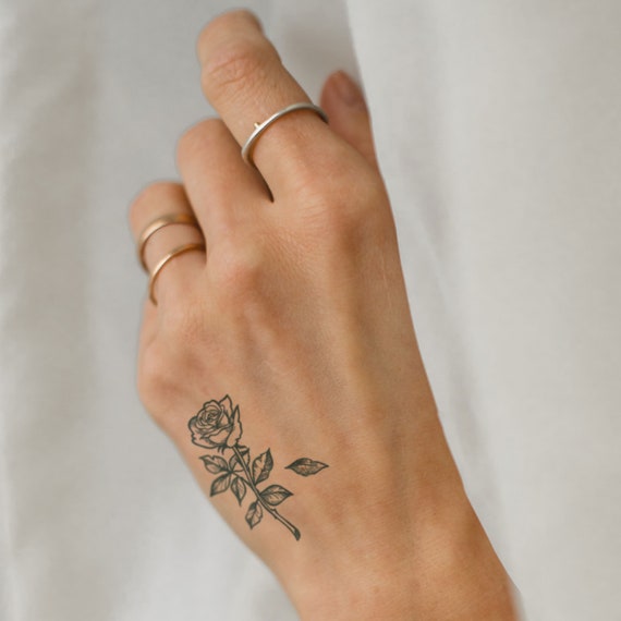 Black and grey shaded rose couple tattoo below right upper thumb