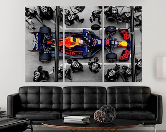May include: A red and blue Formula One race car is being serviced by a pit crew. The car is surrounded by mechanics wearing black uniforms. The car has the words "Red Bull" and "Aston Martin" on it.