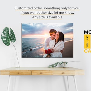 May include: A canvas print featuring a couple embracing on a beach at sunset. The print has a modern design and is available in various sizes.  "MODERN WALL ART CANVAS" is printed in the bottom right corner.