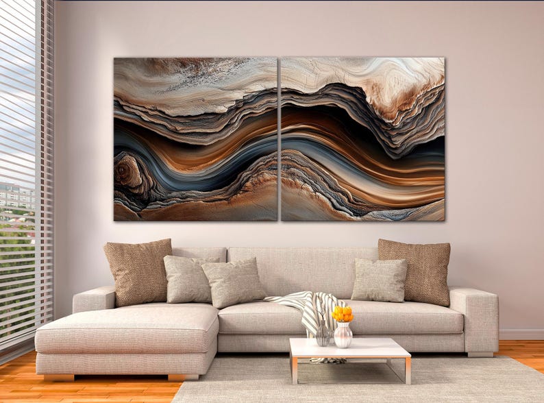 a modern living room with a large abstract painting hanging on the wall above a beige sofa with throw pillows. The sofa is positioned in front of a coffee table with a vase of flowers on it. The room has a wooden floor and a window with blinds, creating a cozy and inviting atmosphere.