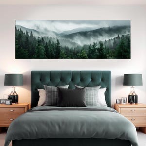 May include: A long canvas print of a misty forest scene is displayed above a bed with a teal headboard and bedding. The print shows a green forest with fog in the valleys. Two wooden bedside tables with lamps are on either side of the bed.