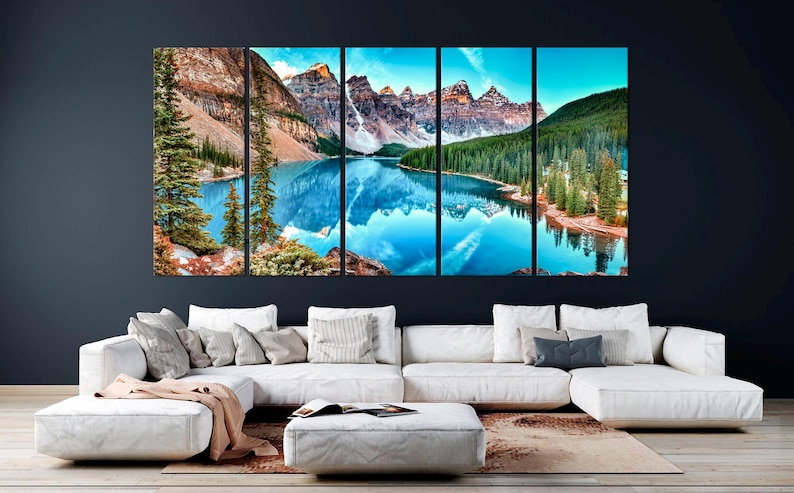May include: A panoramic view of a mountain lake with snow-capped peaks reflected in the water. The lake is surrounded by lush green trees and the mountains are a mix of brown and green.