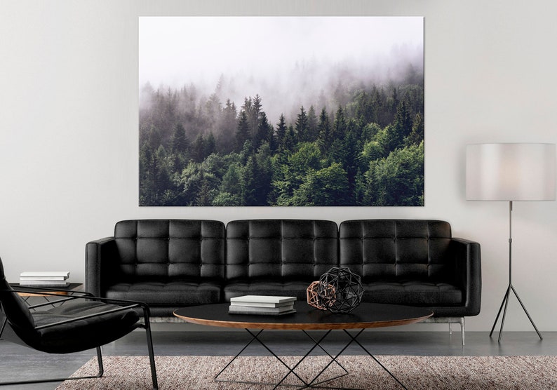 May include: A photograph of a misty forest with tall green trees. The forest is in the background of a living room with a black leather sofa, a round coffee table, and a floor lamp.