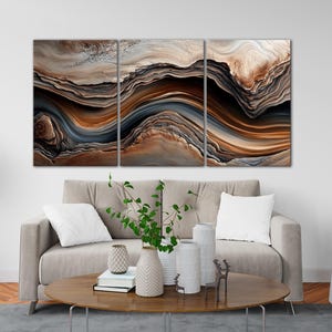 a modern living room with a large abstract painting hanging on the wall above a gray sofa. The sofa is positioned in front of a coffee table, which has decorative items such as vases and books on it. The room also includes a gray armchair and a gray rug, creating a cozy and stylish atmosphere.