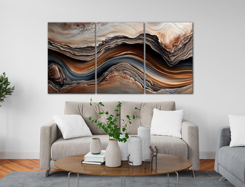 a modern living room with a large abstract painting hanging on the wall above a gray sofa. The sofa is positioned in front of a coffee table, which has decorative items such as vases and books on it. The room also includes a gray armchair and a gray rug, creating a cozy and stylish atmosphere.