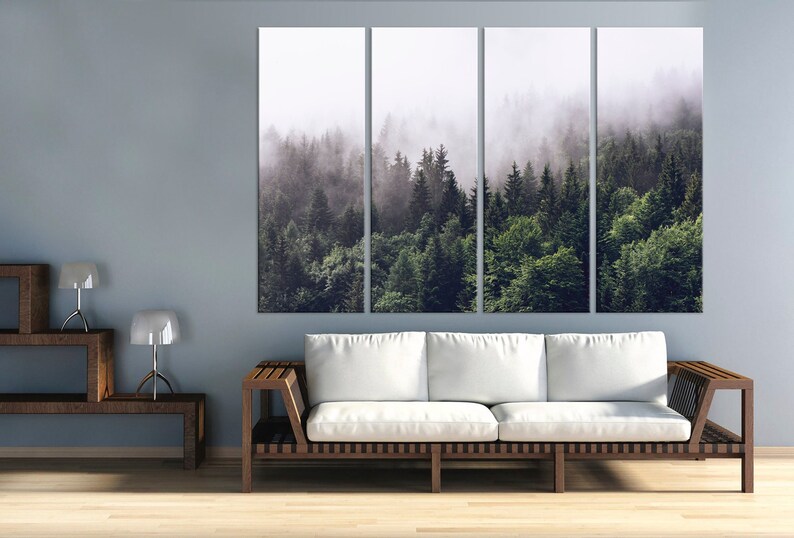 May include: A multi-panel canvas print depicting a misty forest scene. The image shows a dense woodland with tall trees and a layer of fog covering the landscape. The colours are muted greens and greys, creating a serene and atmospheric feel.
