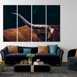 May include: A close-up of a brown and white longhorn steer with large horns. The steer is looking to the right of the frame. The background is dark and blurry.