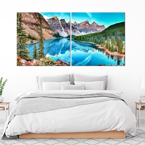 May include: A split canvas print depicting a mountain lake scene with a reflection of the mountains in the water. The lake is a vibrant blue and the mountains are a mix of brown and green. The sky is a light blue with some clouds.