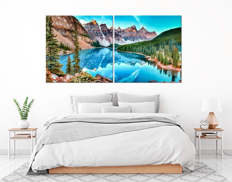 May include: A split canvas print depicting a mountain lake scene with a reflection of the mountains in the water. The lake is a vibrant blue and the mountains are a mix of brown and green. The sky is a light blue with some clouds.