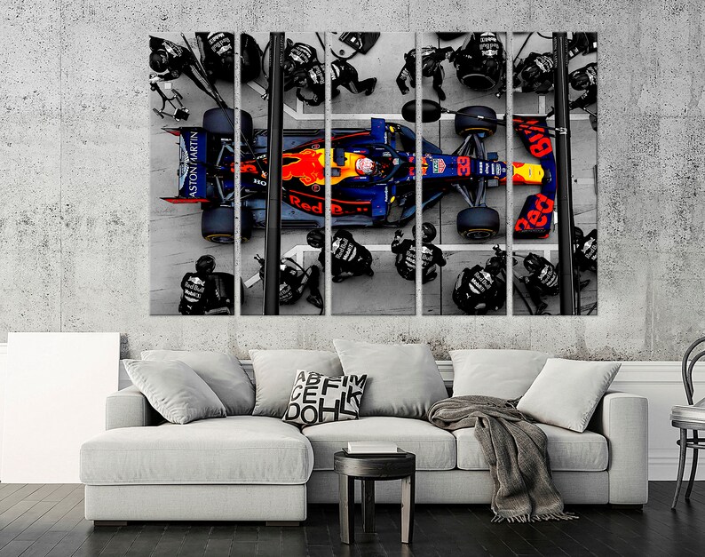 May include: A blue and red Formula One race car with the words "Red Bull" and "Aston Martin" on the side. The car is surrounded by a team of mechanics in black uniforms.