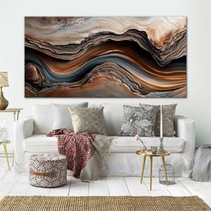 a large abstract painting with a wave-like pattern in shades of brown, orange, and gray, hanging on a white wall above a white sofa with throw pillows.