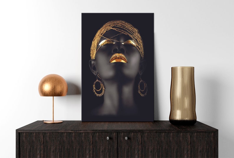May include: A black and gold abstract portrait of a woman with her eyes closed. She is wearing a gold headpiece and large gold earrings. The background is black.