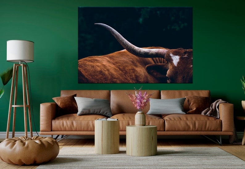 May include: A close-up of a brown and white longhorn steer with large horns. The steer is standing in a dark green field.