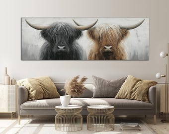 May include: A rectangular canvas print featuring two Highland cows. One cow is black, the other is tan, both with long, shaggy fur and large horns. The background is a muted gray, and the artwork is displayed above a gray sofa.