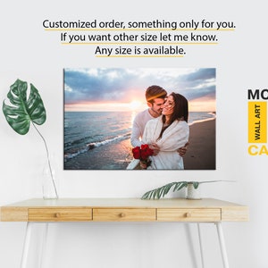 May include: A canvas print depicting a couple embracing on a beach at sunset. The print has a modern design and is available in various sizes. The text "MODERN WALL ART CANVAS" is displayed in the top right corner.