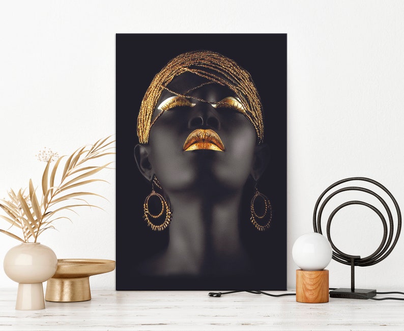 May include: A black and gold portrait of a woman with her eyes closed and lips painted gold. She is wearing a gold beaded headpiece and large gold hoop earrings.